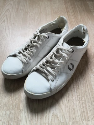 Fred Perry skor - Ett par riktigt klassiska vita sneakers från Fred Perry. De är extremt sällsynta enligt mig för har aldrig sätt en liknade sko från Fred Perry. Skulle säga att de liknar Philipe Model i själva formen av skon förutom märket såklart.                                           Tyvärr lite trasiga i hälen på insidan men inget man känner eller ser när man har på sig dom, har själv bara användt de 2-3 gånger men tyvärr är de förstora. Kan gå ner i pris vid snabb affär.