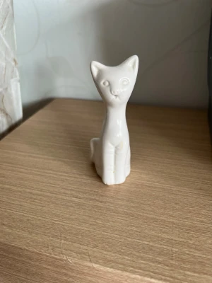 Vit porslinskatt prydnadsfigur - Söt liten prydnadsfigur i form av en sittande katt, tillverkad i vit blankt porslin. Perfekt som dekoration på hyllan eller skrivbordet. Minimalistisk och stilren design som passar in i de flesta hem.