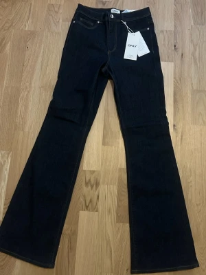 Mörkblå bootcut jeans från ONLY - Snygga mörkblå bootcut jeans från ONLY med klassisk femficksmodell och hög midja. Jeansen har utsvängda ben och är tillverkade i ett stretchigt denimtyg som sitter bekvämt. Perfekta för dig som gillar en retroinspirerad look.