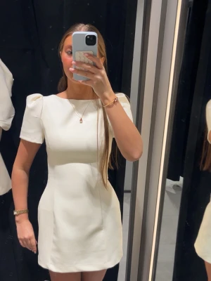 Vit kort puffärmad klänning - Säljer en stilren vit kort klänning med puffärmar och rund hals. Klänningen har en figurnära passform och är perfekt för dig som gillar en enkel men elegant look. Tillverkad i ett mjukt tyg som känns bekvämt mot huden. Aldrig använd men har inte kvar prislappen!!!