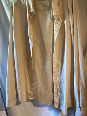 Beige linneskjorta från Growing Star - Säljer en beige skjorta från Growing Star i storlek XL. Skjortan är tillverkad i linne, har klassisk krage, långa ärmar och knäppning framtill. Perfekt för en avslappnad och stilren look.