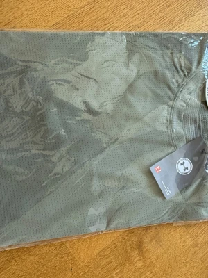 Olivgrön träningströja Under Armour - Säljer en olivgrön träningströja från Under Armour. Tröjan är tillverkad i ett lätt och ventilerande meshmaterial, perfekt för intensiva träningspass. Klassisk rund hals och diskret logga framtill. Snygg och funktionell för gymmet eller löprundan.