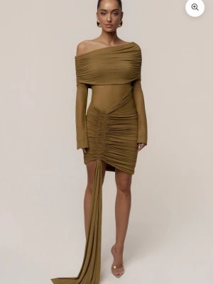 Brun/gul offshoulder klänning - Trendig brun/gul klänning med offshoulder-design och långa ärmar. Klänningen har draperade detaljer och en lång asymmetrisk volang framtill. Tillverkad i ett stretchigt syntetmaterial som sitter snyggt på kroppen. Endast testad av mig köpt på vinted https://jluxlabel.com/sv-ch/products/lime-after-hours-drape-dress