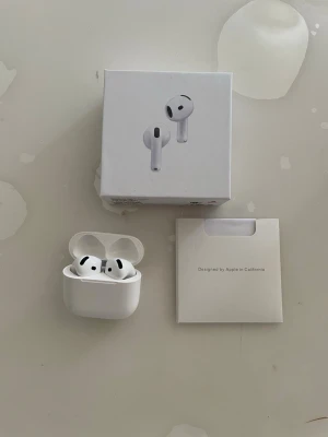 AirPods 4 - Hej Säljer ett par vita trådlösa  hörlurar med laddningsetui, extra silikonpluggar och laddkabel. Hörlurarna har en stilren och modern design med rundade former och touchkontroller på sidan. Perfekt för musik, poddar och samtal. 
