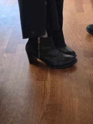 Svarta stövletter med klack och dragkedja - Säljer ett par svarta stövletter i skinnimitation med rundad tå och bred klack. Dragkedja på sidan för enkel på- och avtagning. Snygg och tidlös modell som passar till många olika outfits.  Vet inget om märke tyvärr :((