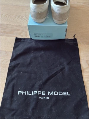 Sneakers från Philippe Model Paris - Snygga sneakers från Philippe Model Paris i beige och vitt. Skorna har en klassisk låg siluett med detaljer i mocka och textil. Kommer med originalpåse och låda. Perfekta för dig som gillar stilrena och exklusiva sneakers. Köpta i mars och endast använd 2 månader. 