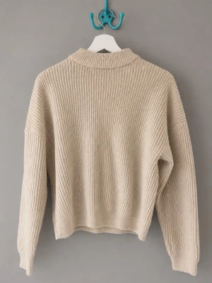 Beige ribbstickad tröja med högre krage - Mysig beige stickad tröja med ribbad struktur och hög krage. Tröjan har avslappnad passform. 
