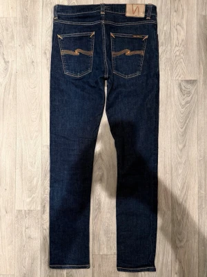 Nudie Jeans Lean Dean Dry Mörkblå W31/L32 - Slim Tapered Fit - Nudie Jeans Lean Dean ”Dry 16 Dips” mörkblå Dry-jeans med slim tapered-passform, normalhög midja och avsmalnande ben, storlek W31/L32, midja 39,5 cm, ytterbenslängd 101 cm, benöppning 15,5 cm, modellen är 185cm & väger 65kg, i fint skick.