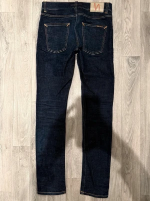 Nudie Jeans Lean Dean Dry Mörkblå W29/L32 - Slim Tapered Fit - Nudie Jeans Lean Dean ”Dry Deep Layers” mörkblå Dry-jeans med slim tapered-passform, normalhög midja och avsmalnande ben, storlek W29/L32, midja 39 cm, ytterbenslängd 105,5 cm, benöppning 15,5 cm, i fint skick.