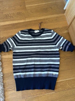 Randig stickad tröja Holly & Whyte - Snygg stickad tröja från Holly & Whyte by Lindex i marinblått och vitt. Tröjan har breda horisontella ränder, rund halsringning och ribbade muddar. Perfekt till jeans eller kjol för en avslappnad look.