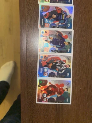 Topps Showboat fotbollskort - Fyra glittriga Topps Showboat fotbollskort med olika spelare i actionposer. Korten har färgstarka bakgrunder och visar spelare i matchställ. Perfekt för samlare eller fotbollsfans som gillar snygga samlarkort.