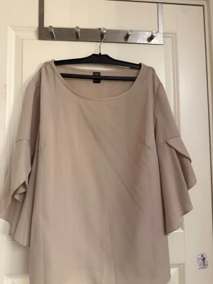 Beige blus med volangärmar - Säljer en beige blus med rund halsringning och vida volangärmar. Blusen har en lös passform och är tillverkad i ett mjukt, lätt material som ger ett snyggt fall. Perfekt för dig som gillar stilrena och feminina plagg.
