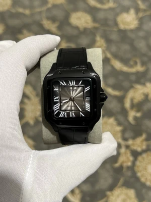 Svart Seiko Santos (AUTOMATISKT) - Stilren svart Seiko klocka med fyrkantigt boett, romerska siffror och automatisk urverk. Klockan har svart läderband och datumvisning. Baksidan har genomskinligt fönster som visar mekaniken. Perfekt för dig som gillar klassisk men modern stil.