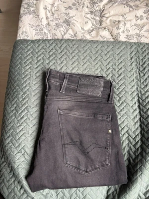 Replay Jeans - Säljer ett par svarta Replay Anbass jeans i storlek 31. Jeansen har klassisk femficksdesign, raka ben och snygga detaljer på bakfickan. Materialet är stretchigt och bekvämt, perfekt för en avslappnad stil.