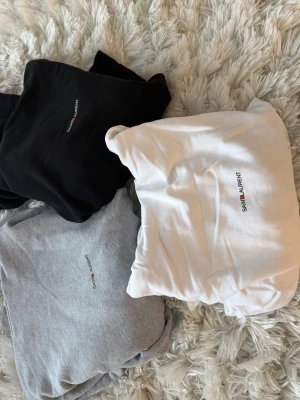 Saint Laurent hoodie i tre färger - Säljer tre stilrena hoodies från Saint Laurent i svart, vitt och grått. Alla har minimalistisk logga på bröstet och klassisk huva med dragsko. Perfekt för dig som gillar enkel och snygg design. Mjukt material och känguruficka framtill. Kan köpas separat!