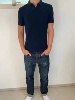 Mörkblå pikétröja - En stilren mörkblå pikétröja med klassisk krage och korta ärmar från dressman. Tröjan har en slim passform och är tillverkad i mjuk bomull. Perfekt till skolstart för en dunder outfit!🙌Storlek S men passar även M.