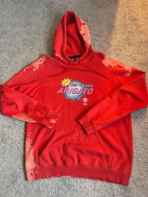 Axel arigato hoodie - Säljer en röd Axel arigato hoodie med japanska tecken. Hoodien har unika blekta detaljer över axlar och ärmar, samt en stor magficka och dragsko i huvan. Perfekt för dig som gillar streetwear och vill sticka ut.