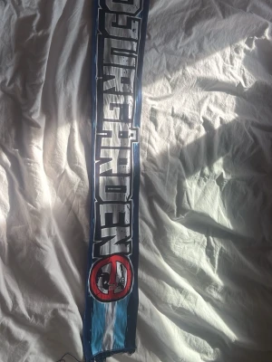 Blå Djurgården supporterscarf - Supporter halsduk i silk i färgerna blått och vitt med texten 'Djurgården' och 'Frihet för ultras' i stora bokstäver. Den har även ett tryck med ett överstruket motiv. Perfekt för dig som vill visa ditt stöd på matchen. Den kommer aldrig att säljas igen och är väldigt unik! Kom med prisförslag 