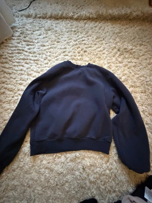 Mörkblå sweatshirt utan huva - En enkel och stilren mörkblå sweatshirt med rund halsringning och långa ärmar. Tröjan har breda muddar vid ärmslut och nederkant. Perfekt för en avslappnad look och lätt att matcha med jeans eller mjukisbyxor.
