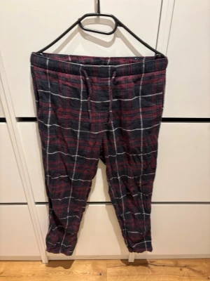 Rutiga pyjamasbyxor i rött och blått - Mysiga pyjamasbyxor i mjukt tyg med röd och mörkblå rutig design samt vita linjer. Byxorna har resår i midjan och dragsko för bästa passform. Perfekta för chillkvällar hemma eller när du vill vara extra bekväm.