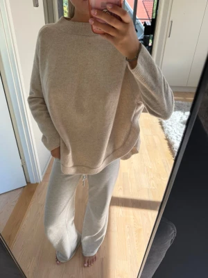 Beige oversized stickad kashmir tröja - Mysig beige oversized stickad tröja med hög hals och slapp passform. Tröjan har långa ärmar och ribbade muddar vid hals, ärmslut och nederkant. Perfekt för en chill och avslappnad stil.