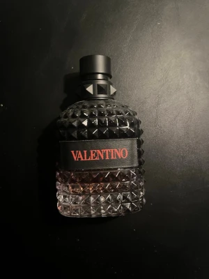 Valentino parfym coral fantasy - Säljer en lyxig parfym från Valentino i en cool, nitprydd glasflaska med svart och transparent design. Flaskan har en svart etikett med röd text och ett unikt lock med nitar. Perfekt för dig som gillar exklusiva dofter och snygg design. Den är 75% full.