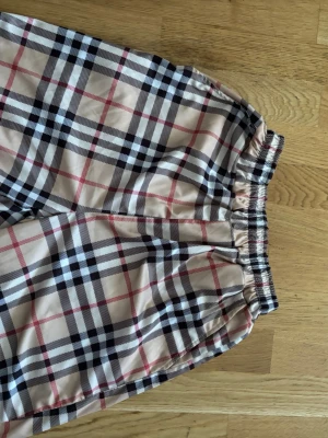 Beige rutiga shorts med resårmidja - Snygga beige shorts med klassiskt rutigt mönster i svart, vitt och rött. Shortsen har en bekväm resår i midjan och är tillverkade i ett lätt material som passar perfekt till varmare dagar. Stilen är loose fit och de har en avslappnad vibe.