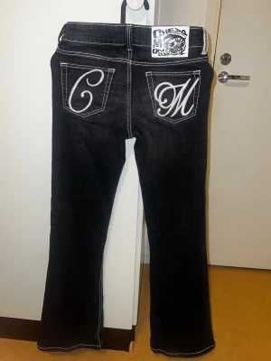 Svarta bootcut jeans med brodyr - Snygga svarta jeans med vita kontrastsömmar och broderade bokstäver på bakfickorna. Bootcut-modell med låg midja. Säljer pga att de inte passar i midjan. Nypris ca 420 kr!! 💗💗 Använd högst 4 ggr💗
