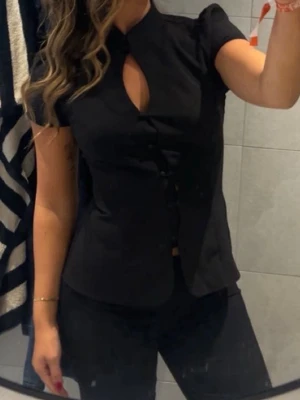 Svart blus med knappdetaljer - Snygg svart blus med korta ärmar och ståkrage. Endast använd 1 gång 💗