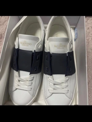 Valentino Garavani  - Snygga vita sneakers från Valentino Garavani med bred svart detalj över snörningen. Skorna har klassisk låg profil, vita snören och sula i gummi. Tillverkade i slätt läder för en clean och exklusiv look