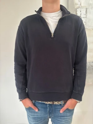 Svart halvzip sweatshirt - En stilren svart sweatshirt med halv dragkedja och hög krage. Tröjan har långa ärmar, ribbade muddar och en avslappnad passform. Perfekt att slänga på sig över en t-shirt för en casual look.