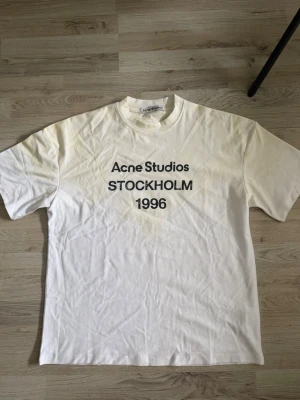Vit Acne Studios t-shirt Stockholm - Vit t-shirt från Acne Studios med svart text 'STOCKHOLM 1996' på bröstet. Klassisk passform och rund halsringning. Perfekt basic-plagg med stilren design och tydlig logga framtill.