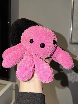 Virkad spindel - Säljer ett gulligt mjukisdjur i form av en spindel med fluffig rosa kropp och ben samt en stor svart bakdel. Spindeln har svarta plastögon och är tillverkad i mjukt garn. Soft Velvet.