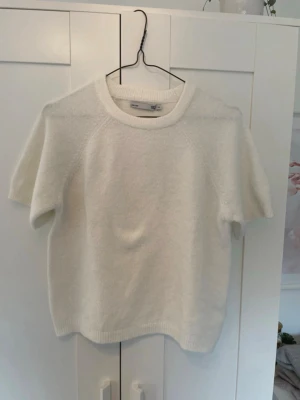 Vit stickad t-shirt från H&M - Kortärmad stickad t-shirt i mjukt vitt material från Lager 157. Tröjan har rund halsringning, ribbade kanter och en enkel, clean look som passar till det mesta. Perfekt för dig som gillar minimalistisk stil och vill ha något bekvämt och snyggt. Det är barn storlek så det är storlek 140