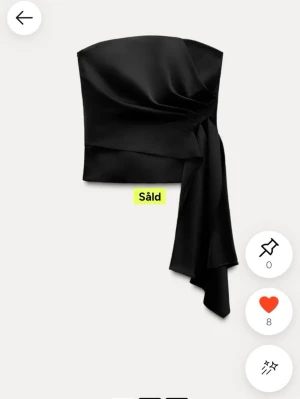 Svart axelbandslös topp med drapering - Trendig svart axelbandslös topp i glansigt satintyg med snygg drapering och asymmetrisk detalj framtill. Perfekt för att lyfta vilken outfit som helst med sin eleganta och moderna look. Den är lite lite trasig på ett ställe men det är inget man ser eller tänker på när man har på sig den☺️