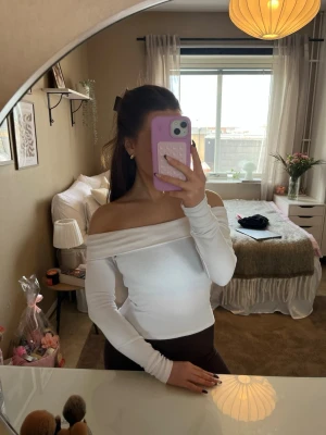 Vit offshoulder långärmad topp - Snygg vit offshoulder topp med långa ärmar och figurnära passform. Perfekt för dig som vill ha en stilren och trendig look. Toppens axelbandslösa design ger en modern vibe och passar till många olika outfits.