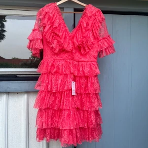 By Malina klänning - Superfin By Malina klänning i fin korallfärg. Helt ny med lappar kvar! Tyget har troligtvis fastnat i dragkedjan någon gång då tyget är lite ruggat där, men det är ingenting som syns när klänningen är på då volangerna får det att smälta in. Modellen heter ”Sky v-neck frill mini lace dress” och nypriset är 2800kr. Kom gärna med prisförslag!