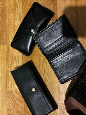 Plånböcker och glasögonfodral  - Säljer två plånböcker och två glasögonfodral i svart och brunt läder. Säljer pga flytt. Allt säljs tillsammans! 25kr för allt