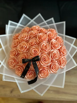 Bukett med konstgjorda rosor  - Säljer en exklusiv bukett med konstgjorda rosor i persikofärg, vackert arrangerade i lager av vit plastfolie och dekorerad . Perfekt som present eller dekoration till hemmet.