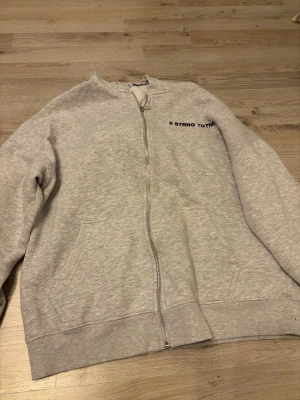 Ljusgrå zip hoodie - Ljusgrå hoodie med dragkedja. Klassisk modell med huva, två fickor framtill och ribbade muddar vid ärmslut och nederkant. Tillverkad i mjukt sweatshirtmaterial, perfekt för en avslappnad stil.