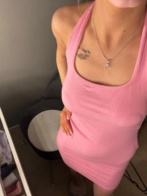 Rosa ribbad kort klänning - Säljer en söt rosa ribbad klänning med halterneck och tight passform. Klänningen är kort och ärmlös, perfekt för varma dagar eller när du vill känna dig extra snygg. Materialet är stretchigt och följsamt för en bekväm känsla.