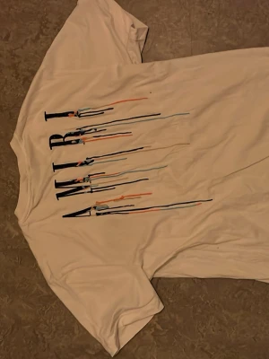 Vit AMIRI t-shirt med färgstänk - Säljer en vit t-shirt från AMIRI med tryck i svart och färgglada stänk på både bröstet och ryggen. T-shirten har en avslappnad passform och är kortärmad. Perfekt för dig som gillar streetwear och vill sticka ut med cool design.