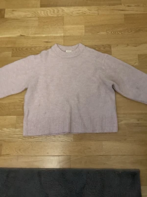 Ljuslila stickad tröja för barn  - Mysig ljuslila stickad tröja med rund halsringning och ribbade muddar vid ärmslut och nederkant. Tröjan har en boxy passform och är perfekt för lager på lager. Materialet ser ut att vara mjukt och skönt, troligen ull- eller bomullsblandning.