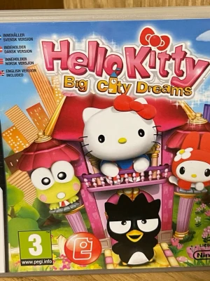 Hello Kitty Big City Dreams DS-spel - Hello Kitty Big City Dreams är ett färgglatt Nintendo DS-spel där du följer Hello Kitty och hennes vänner på äventyr i storstaden. Omslaget har en rosa och blå design med söta figurer och spelet är på flera språk. Perfekt för dig som gillar gulliga och roliga spel.