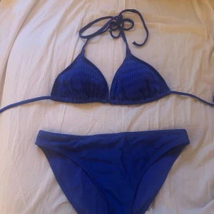 Blå trekantsbikini med knyt - Snygg blå bikini med trekantsöverdel och knyt i nacken och ryggen. Klassisk modell med matchande bikinitrosa i samma färg. Perfekt för stranden eller poolen. Enkel och stilren design som passar till allt.
