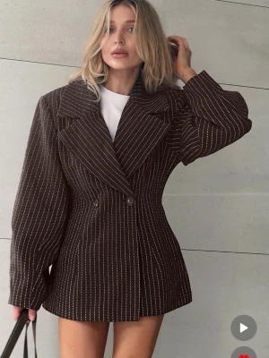 Brun oversize kavaj (slutsåld på hemsidan) - Snygg brun kavaj i oversize-modell med vita kritstrecksränder och breda slag. Dubbelknäppt framtill och långa ärmar. Storlek 34 