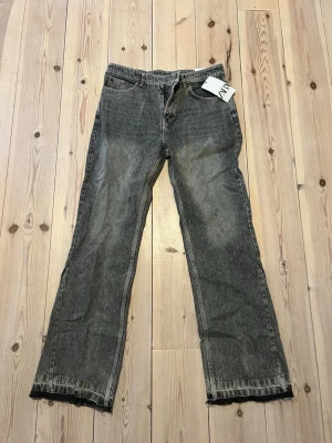Grå flared jeans från Zara - Säljer ett par grå flared jeans från Zara med klassisk femficksmodell och råa, fransiga benslut. Jeansen har en avslappnad passform och är tillverkade i denim med tvättad look. Perfekta för en casual och trendig stil.