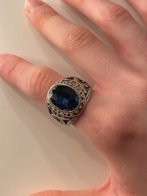 Silverring med blå sten - Snygg silverfärgad ring med en stor, oval slipad blå sten i mitten. Ringen har detaljerade mönster längs sidorna som ger en vintagekänsla. Ej äkta silver och helt oanvänd 🫶