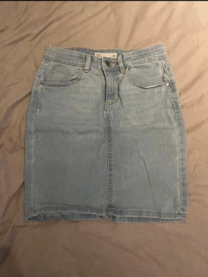 Ljusblå jeanskjol från Cubus  - Säljer en ljusblå jeanskjol från Cubus i klassisk femficksmodell. Kjolen har normal passform, bälteshällor och knapp- samt dragkedjestängning framtill. Perfekt till sommaren och enkel att matcha med olika toppar.