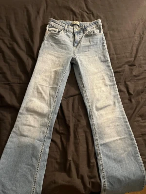 Ljusblå bootcut jeans från ONLY - Säljer ett par ljusblå bootcut jeans från ONLY med klassisk femficksdesign och snygga bakfickor med lock och knapp. Jeansen har normal passform och är tillverkade i bomull med en skön stretch. Supersköna jeans!